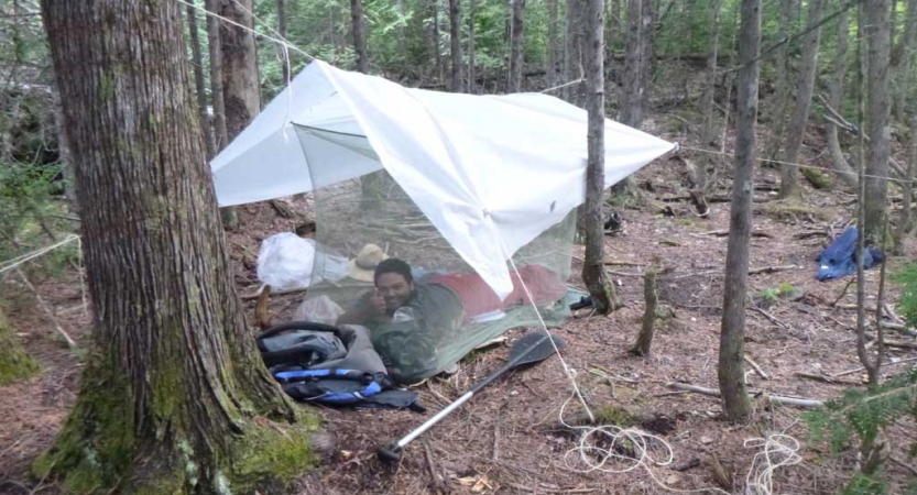 a person smiles while laying under a tarp in the woods on an outward bound expedition 